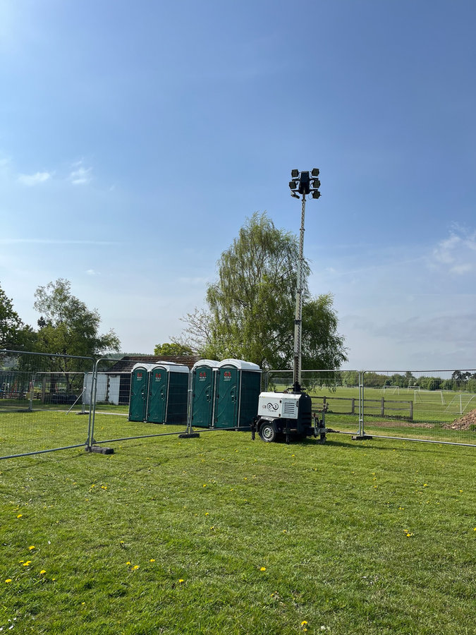 Raised light tower beside portable toilets at an outdoor event site